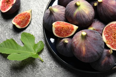 Photo of Whole and cut ripe figs with leaf on light grey textured table, flat lay