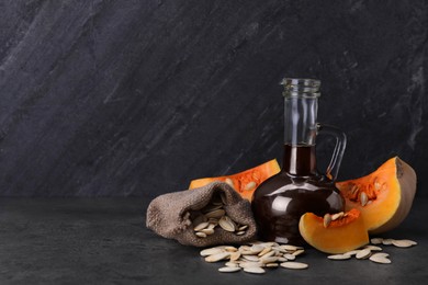 Photo of Fresh pumpkin seed oil in glass jug on dark grey table. Space for text