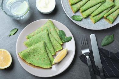 Tasty spinach crepes served on grey table, flat lay