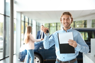 Photo of Salesman with clipboard and car keys in modern auto dealership