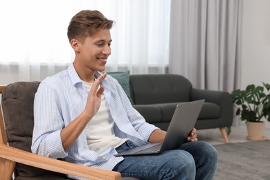 Happy young man having video chat via laptop on armchair indoors