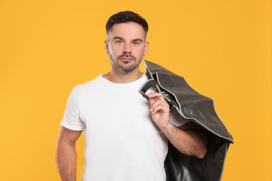 Photo of Man holding garment cover with clothes on yellow background. Dry-cleaning service