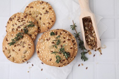 Photo of Cereal crackers with flax, sesame seeds, thyme and scoop on white tiled table, top view