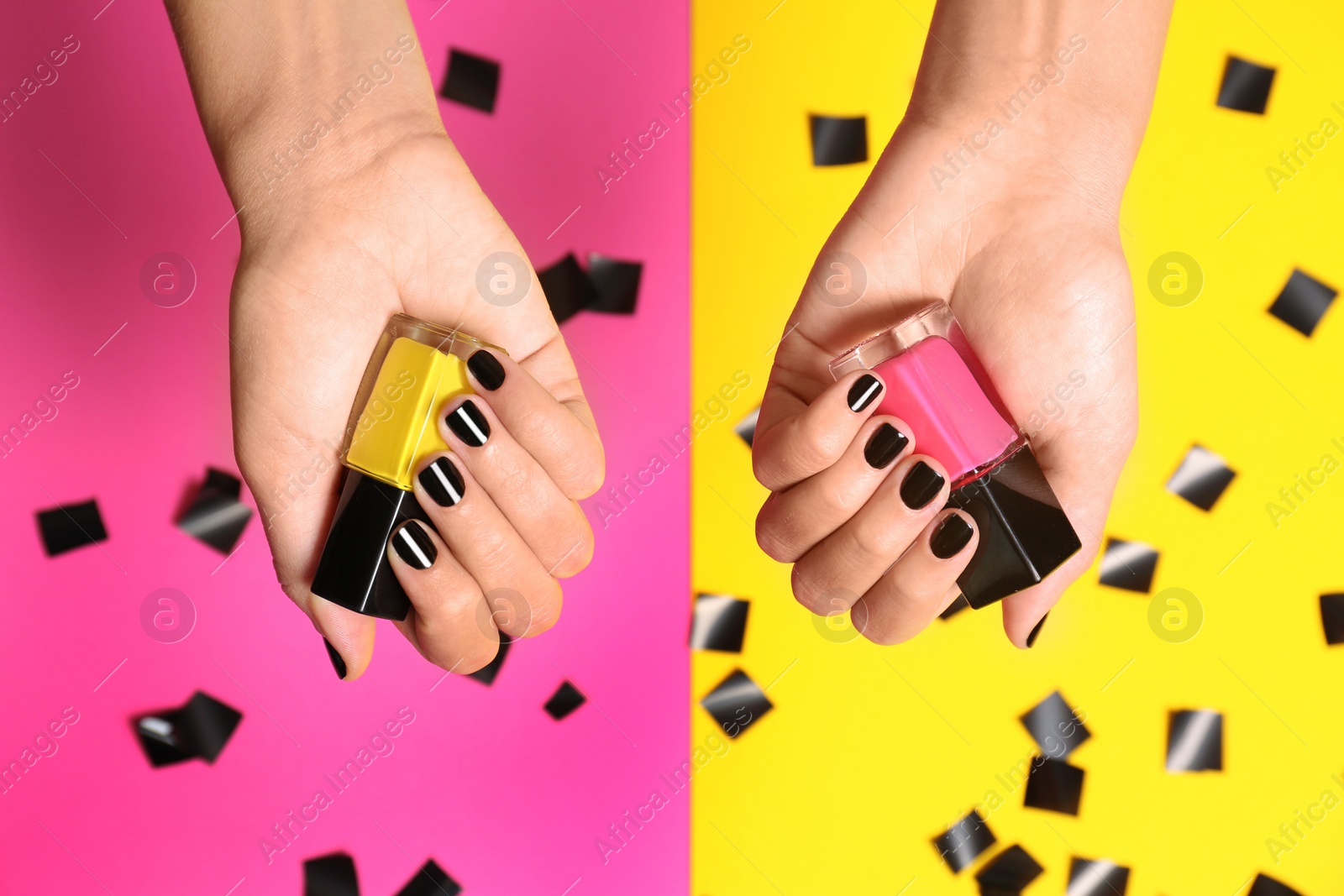 Photo of Woman with black manicure holding nail polish bottles on color background, top view