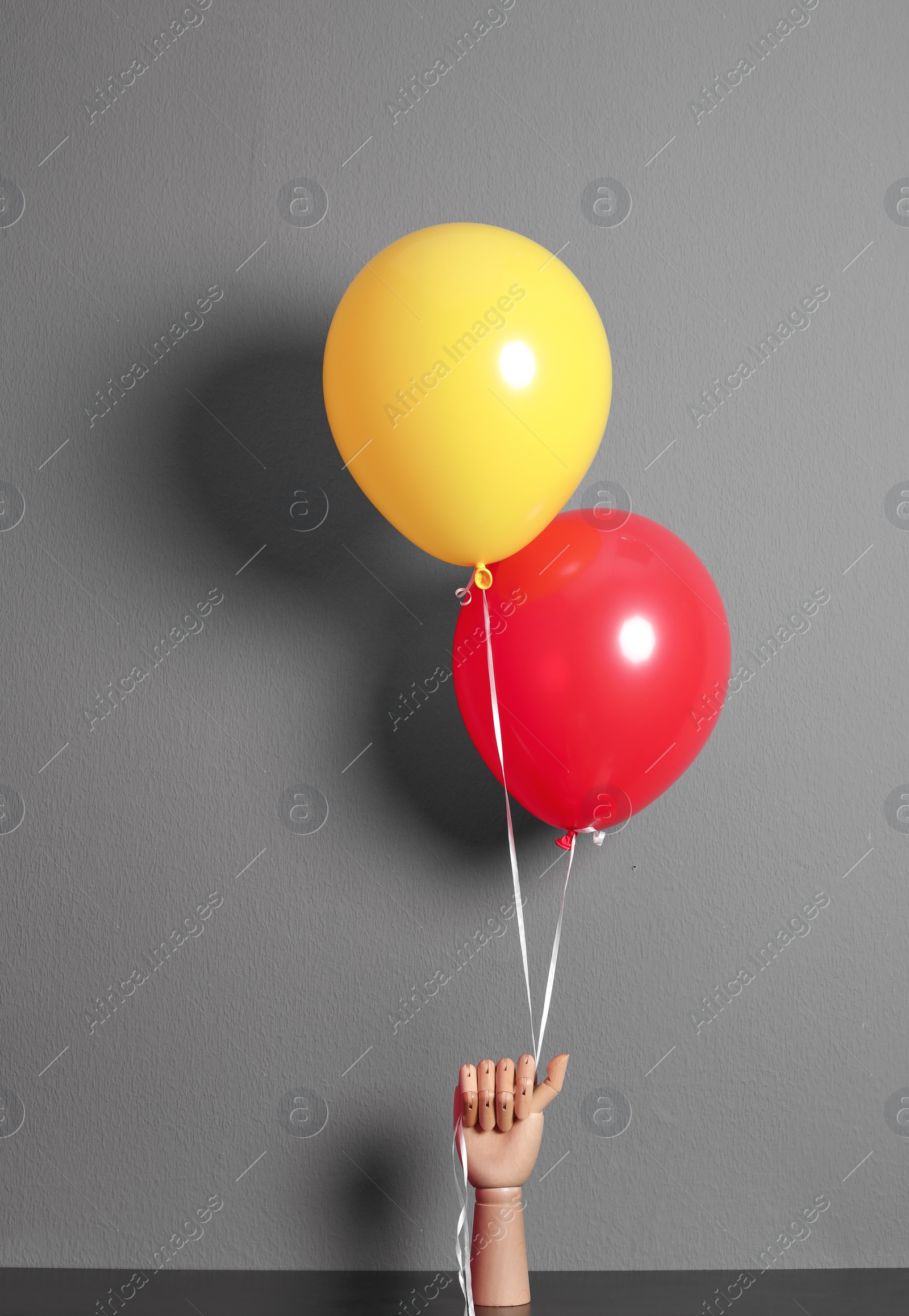 Photo of Wooden hand holding colorful balloons on gray background