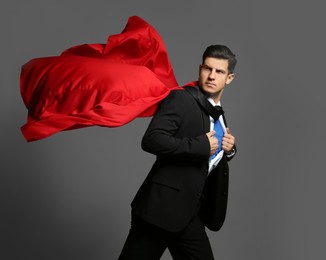 Photo of Businessman in superhero cape taking suit off on grey background