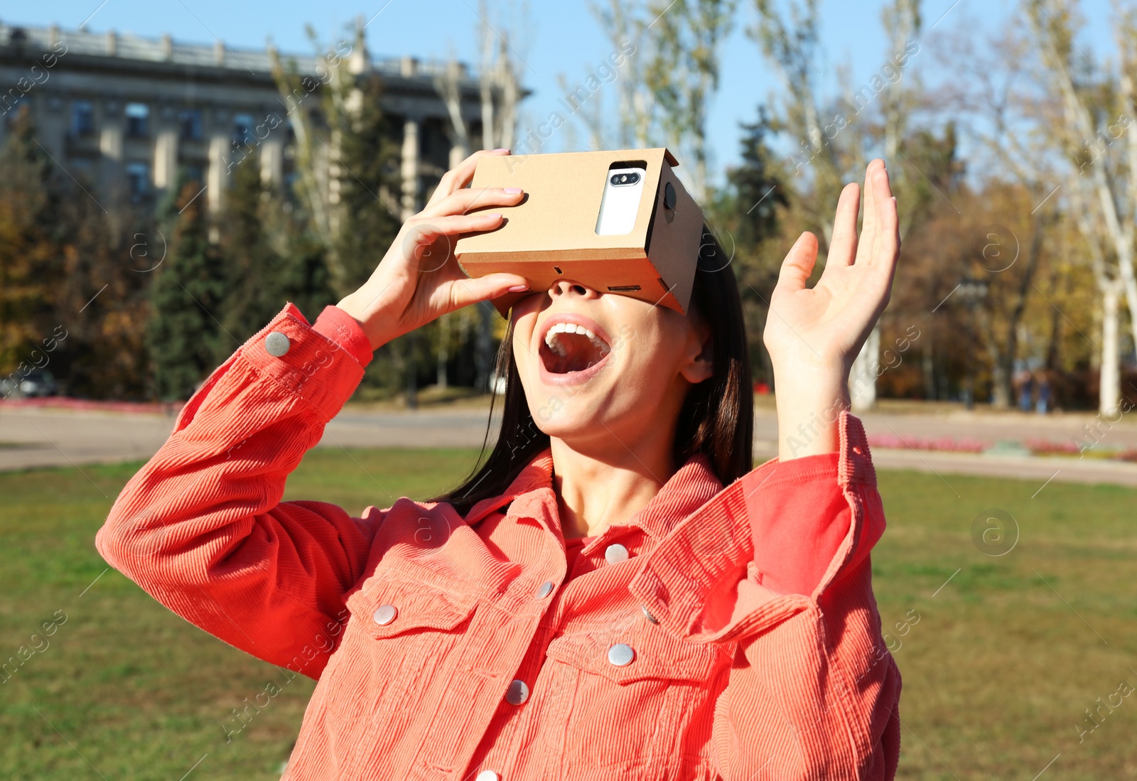 Photo of Young woman using cardboard virtual reality headset outdoors