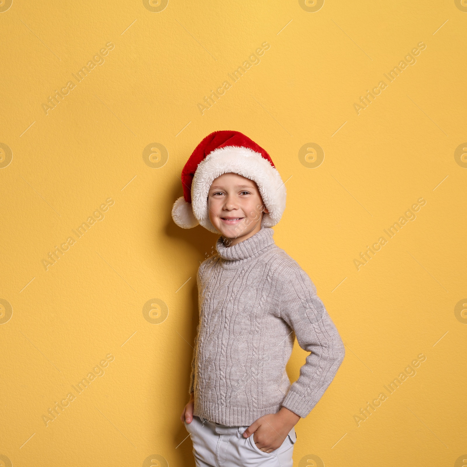 Photo of Cute little boy in warm sweater and Christmas hat on color background