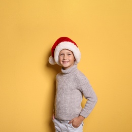 Photo of Cute little boy in warm sweater and Christmas hat on color background