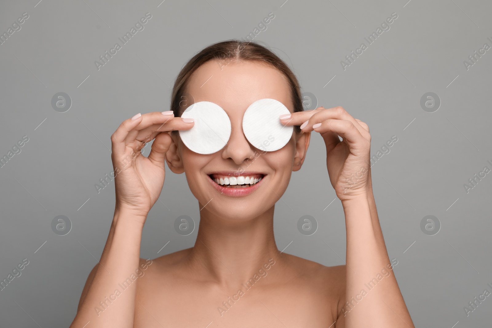 Photo of Smiling woman removing makeup with cotton pads on grey background