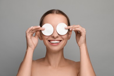 Smiling woman removing makeup with cotton pads on grey background