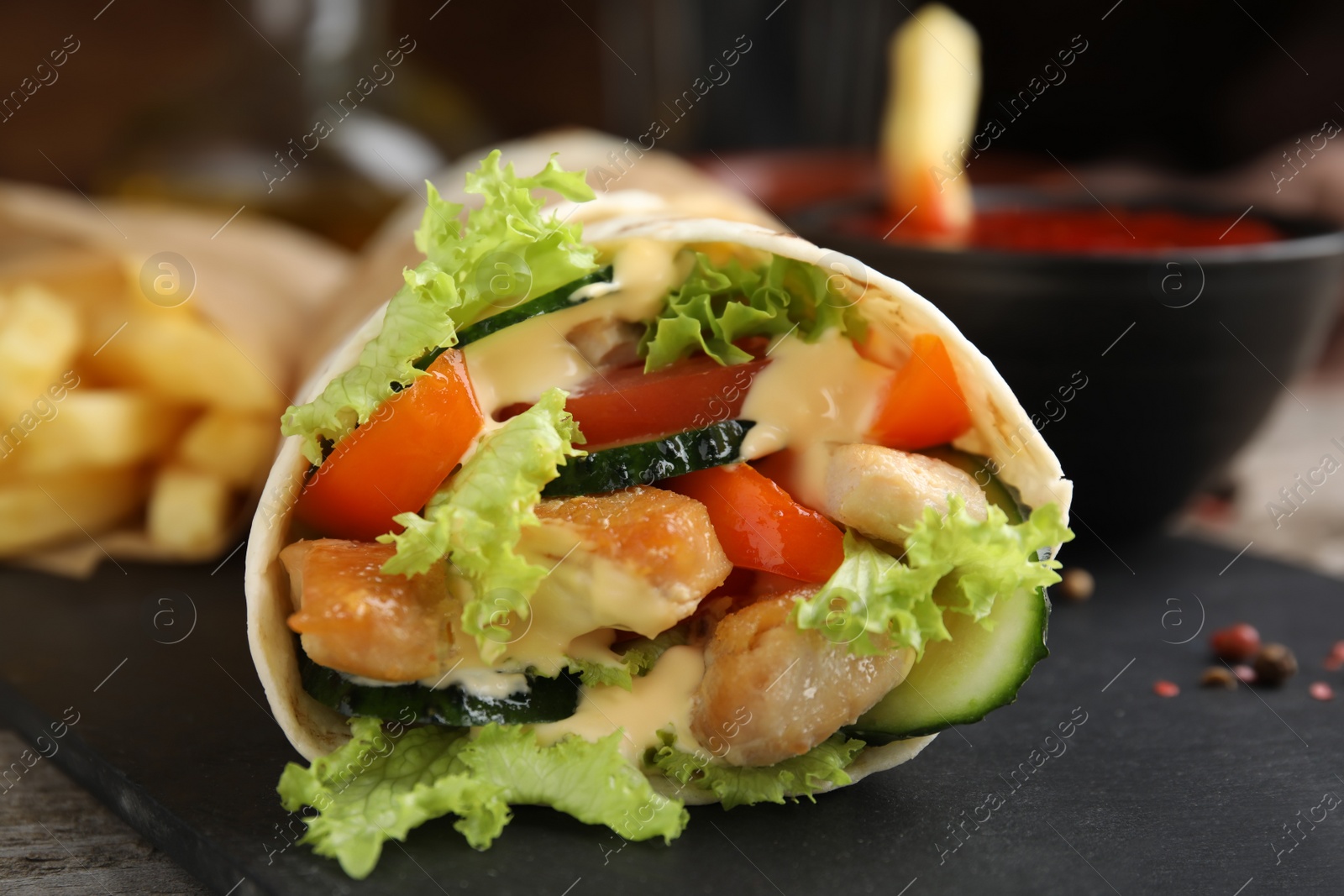 Photo of Delicious shawarma with chicken and fresh vegetables   on slate plate, closeup