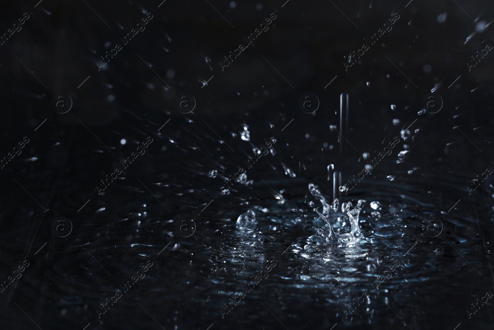 Photo of Rain drop falling down into puddle on dark background