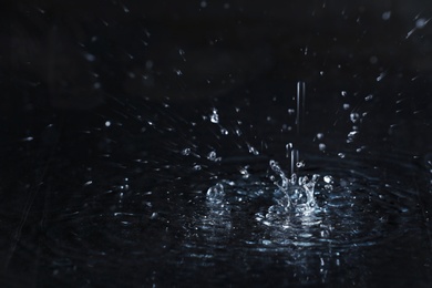 Photo of Rain drop falling down into puddle on dark background