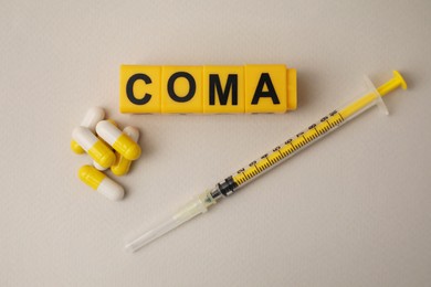 Photo of Word Coma of cubes, syringe and pills on beige background, flat lay