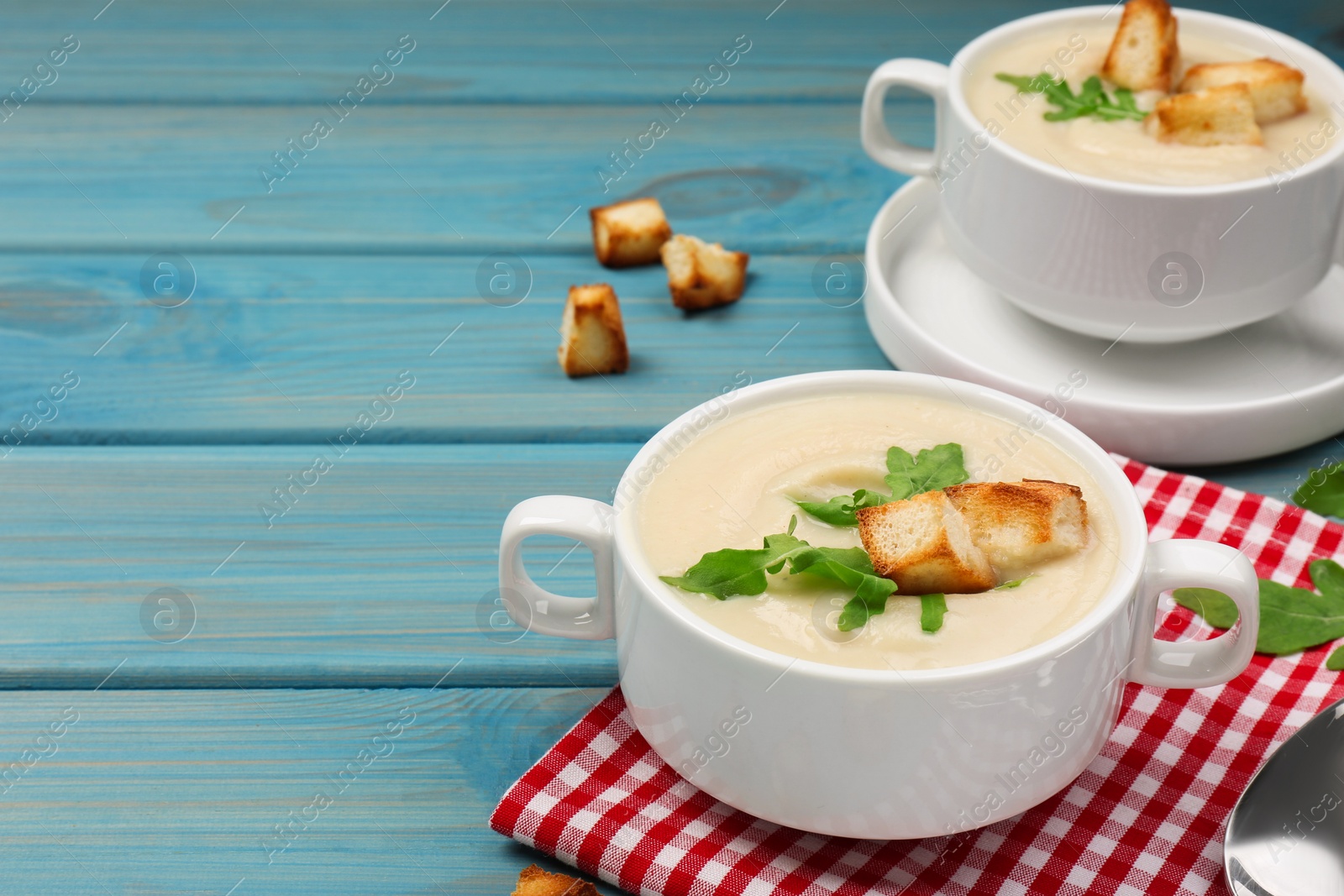 Photo of Bowls with tasty creamy soup of parsnip on light blue wooden table, space for text