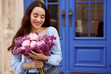 Photo of Beautiful woman with bouquet of spring flowers near building outdoors, space for text