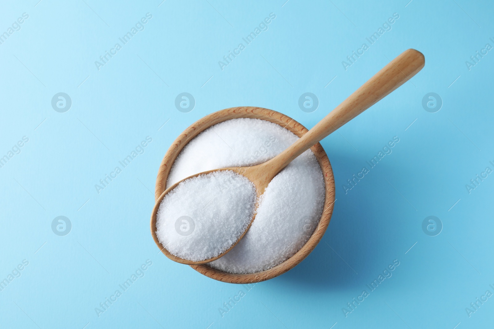 Photo of Organic white salt in bowl and spoon on light blue background, top view