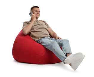 Photo of Handsome man talking by smartphone on red bean bag chair against white background