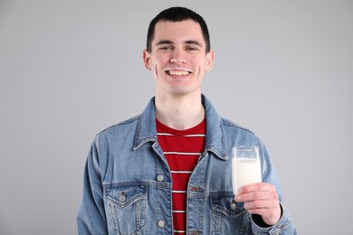 Happy man with milk mustache holding glass of tasty dairy drink on gray background