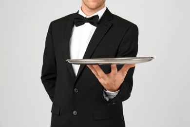 Waiter holding metal tray on light background