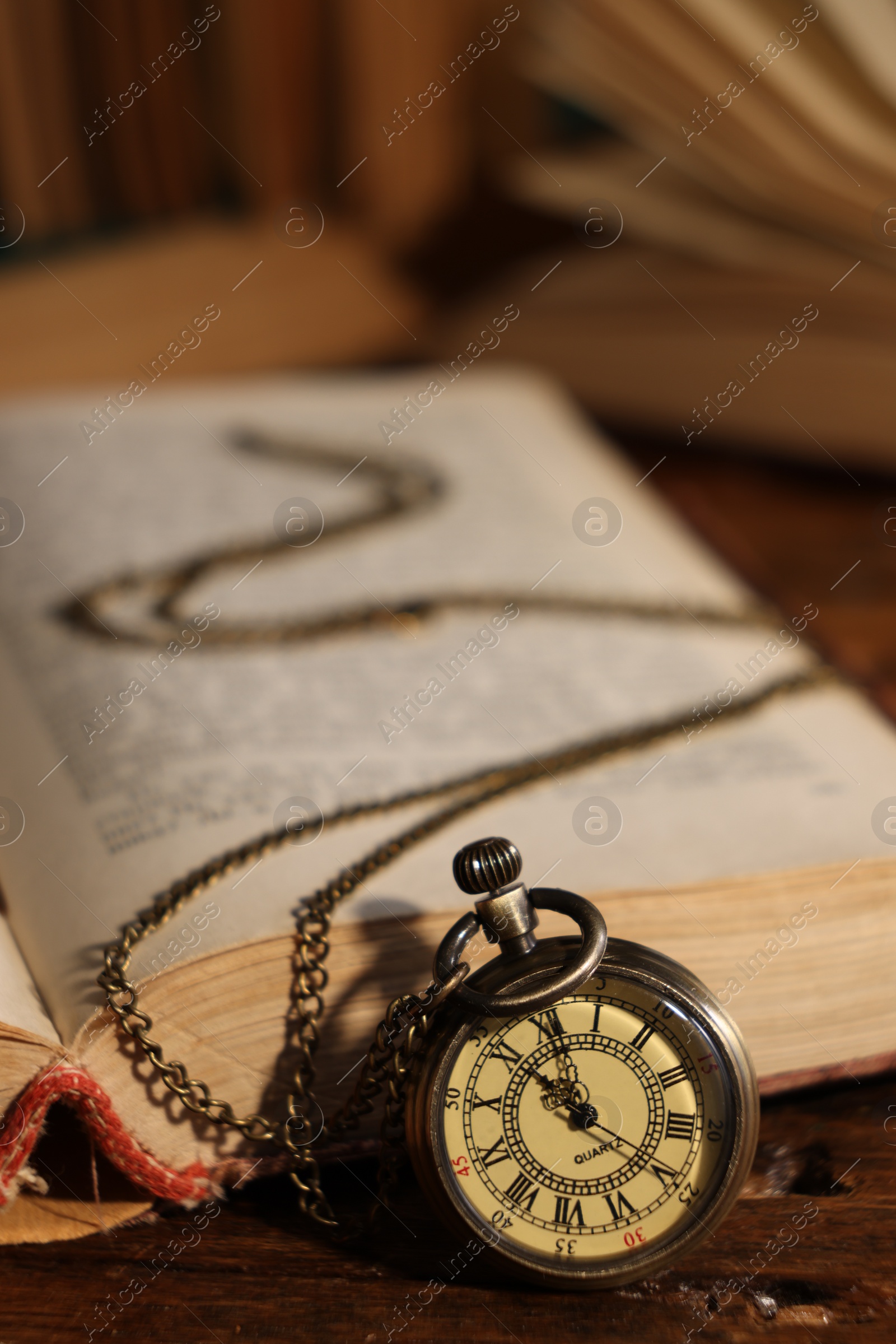 Photo of Pocket clock with chain and book on table, closeup