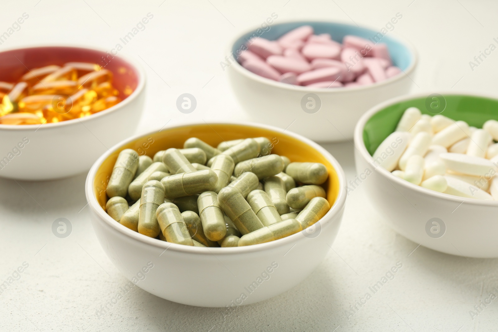 Photo of Different vitamin capsules in bowls on white wooden table, closeup