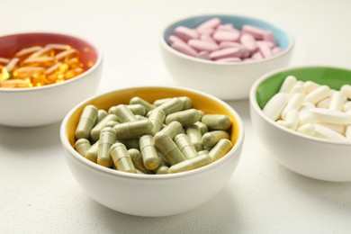 Different vitamin capsules in bowls on white wooden table, closeup