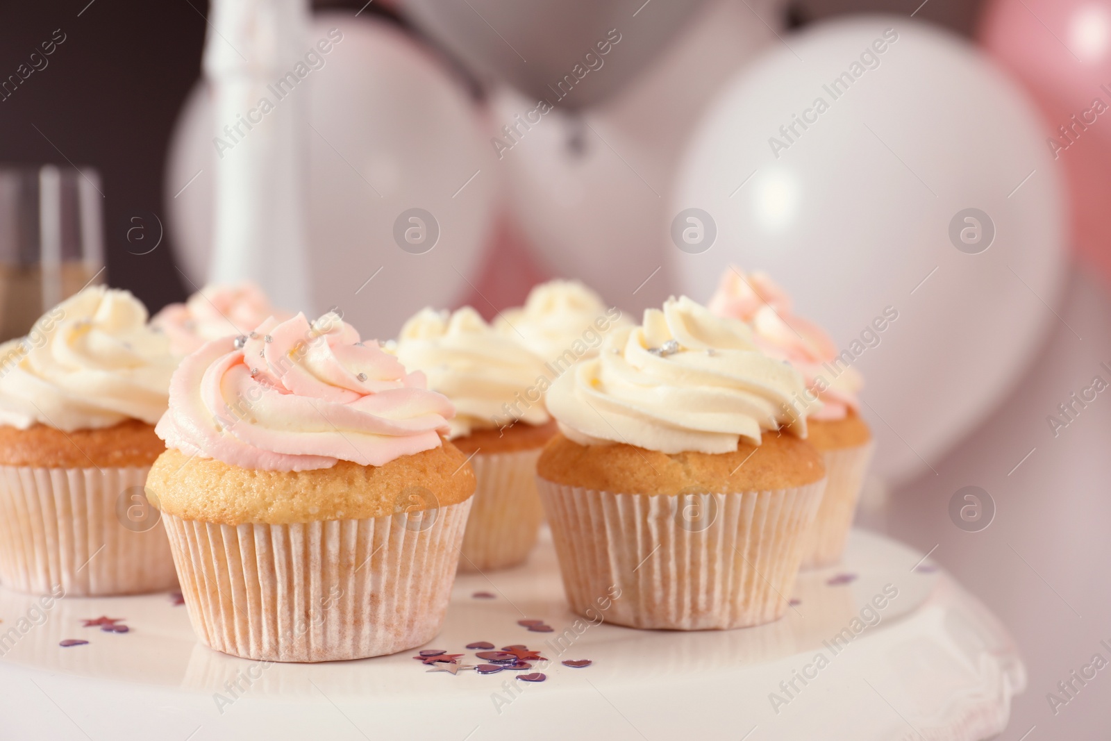 Photo of Stand with cupcakes and blurred balloons on background, closeup