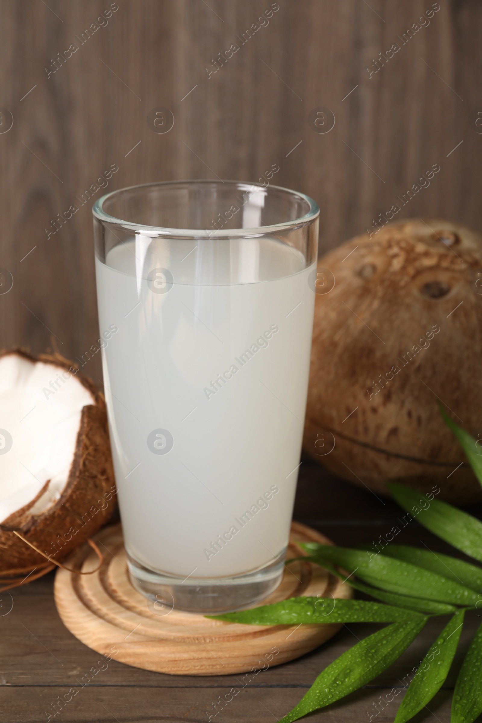 Photo of Glass of coconut water, leaf and nuts on wooden table