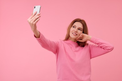 Beautiful woman taking selfie on pink background