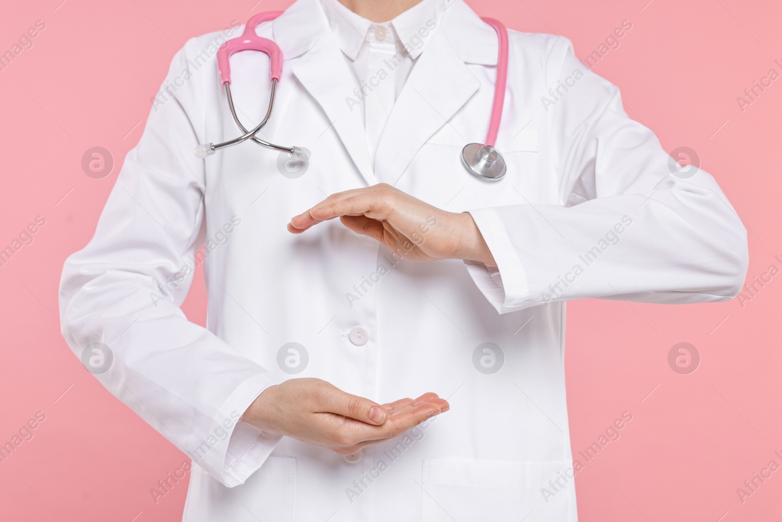 Photo of Doctor with stethoscope holding something on pink background, closeup