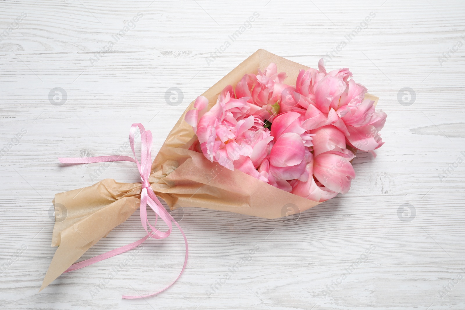 Photo of Beautiful bouquet of pink peonies wrapped in paper on white wooden table, top view