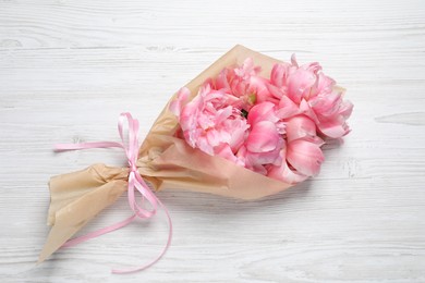 Beautiful bouquet of pink peonies wrapped in paper on white wooden table, top view