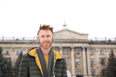 Photo of Young man listening to music with headphones outdoors. Space for text