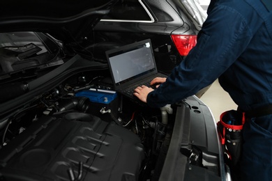 Technician checking car with laptop at automobile repair shop, closeup
