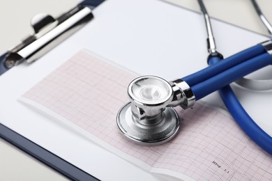 Photo of Stethoscope, clipboard and cardiogram paper on beige background, closeup