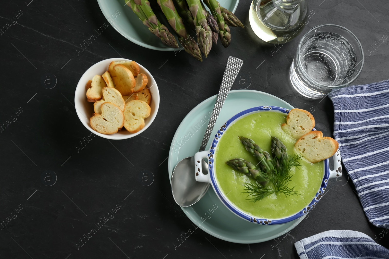 Photo of Delicious asparagus soup served on black table, flat lay