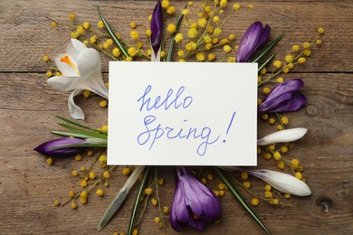 Card with words HELLO SPRING and fresh flowers on wooden table, flat lay