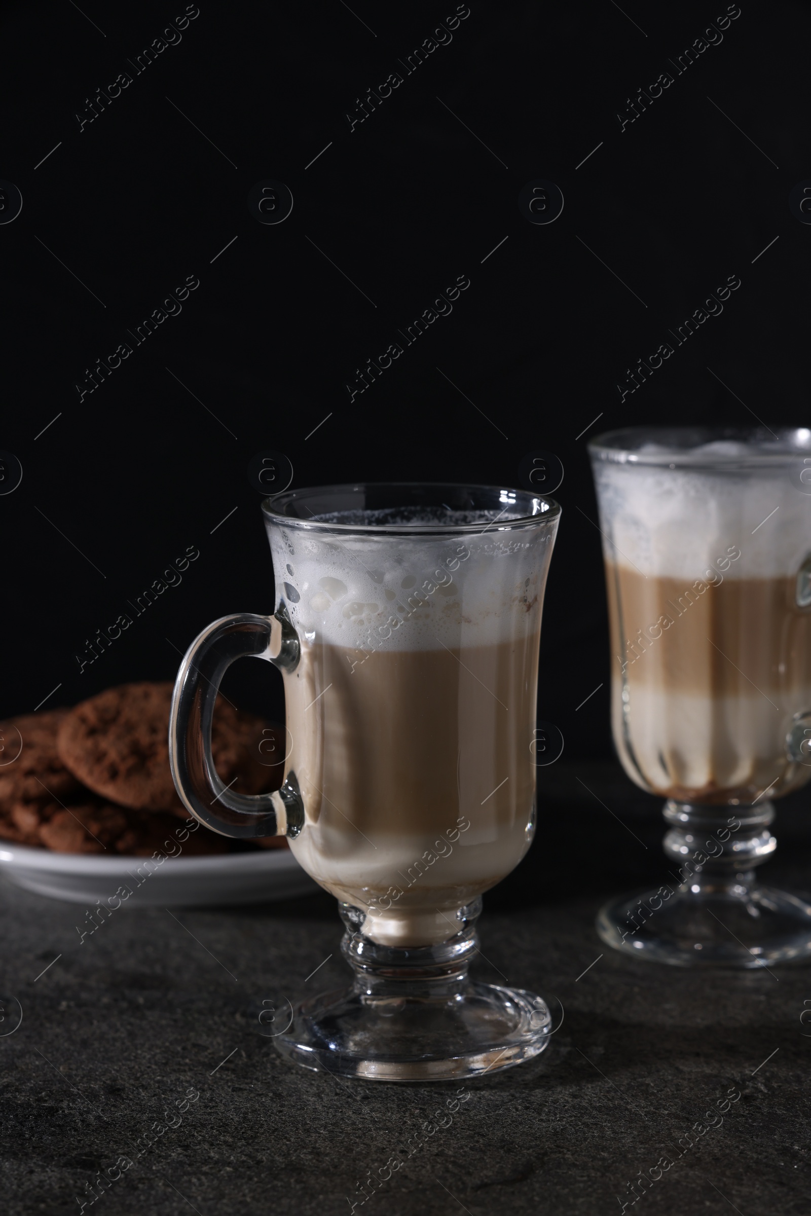 Photo of Aromatic latte macchiato in glasses and chocolate cookies on dark grey table