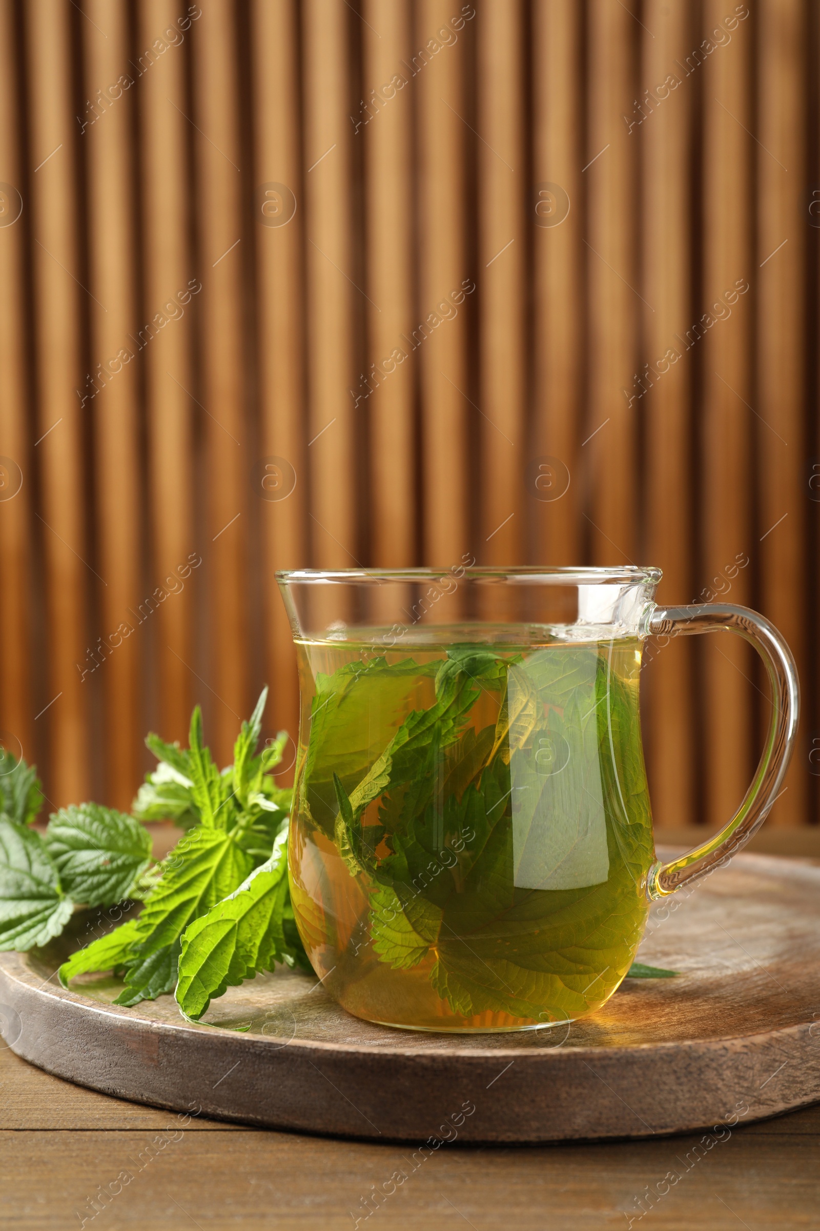 Photo of Glass cup of aromatic nettle tea and green leaves on wooden table