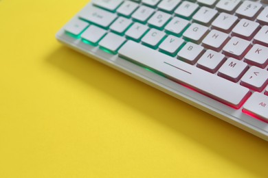 Photo of Modern RGB keyboard on yellow background, closeup. Space for text