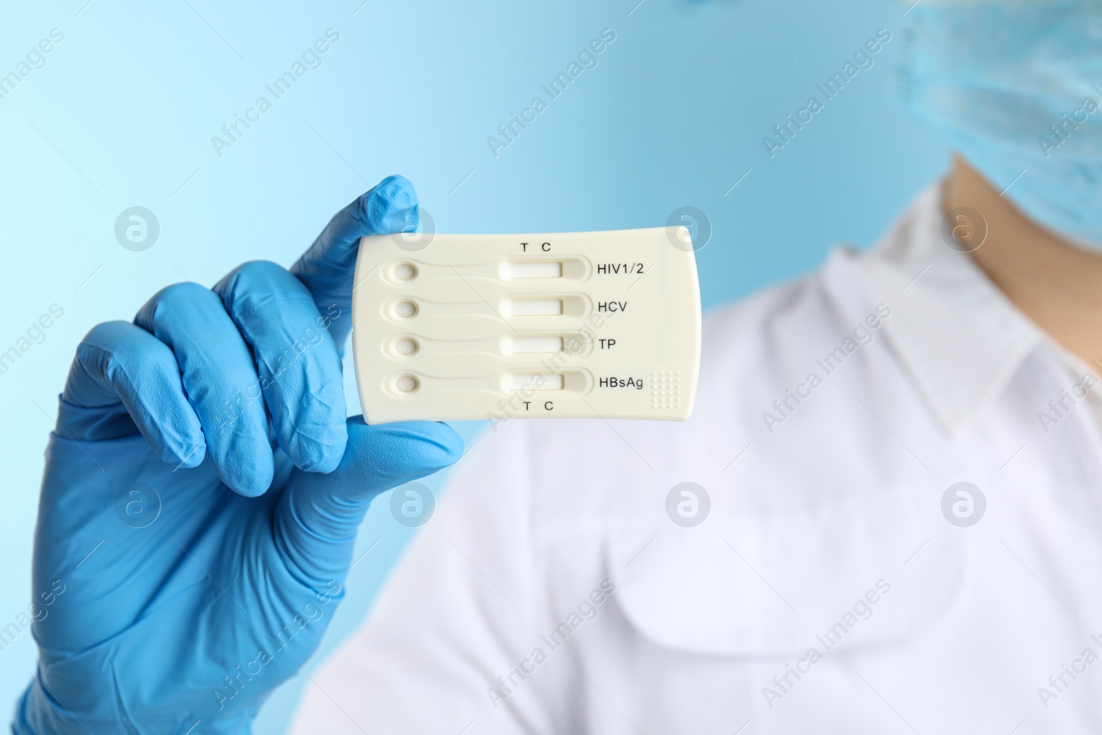 Photo of Doctor holding disposable express test for hepatitis on light blue background, closeup