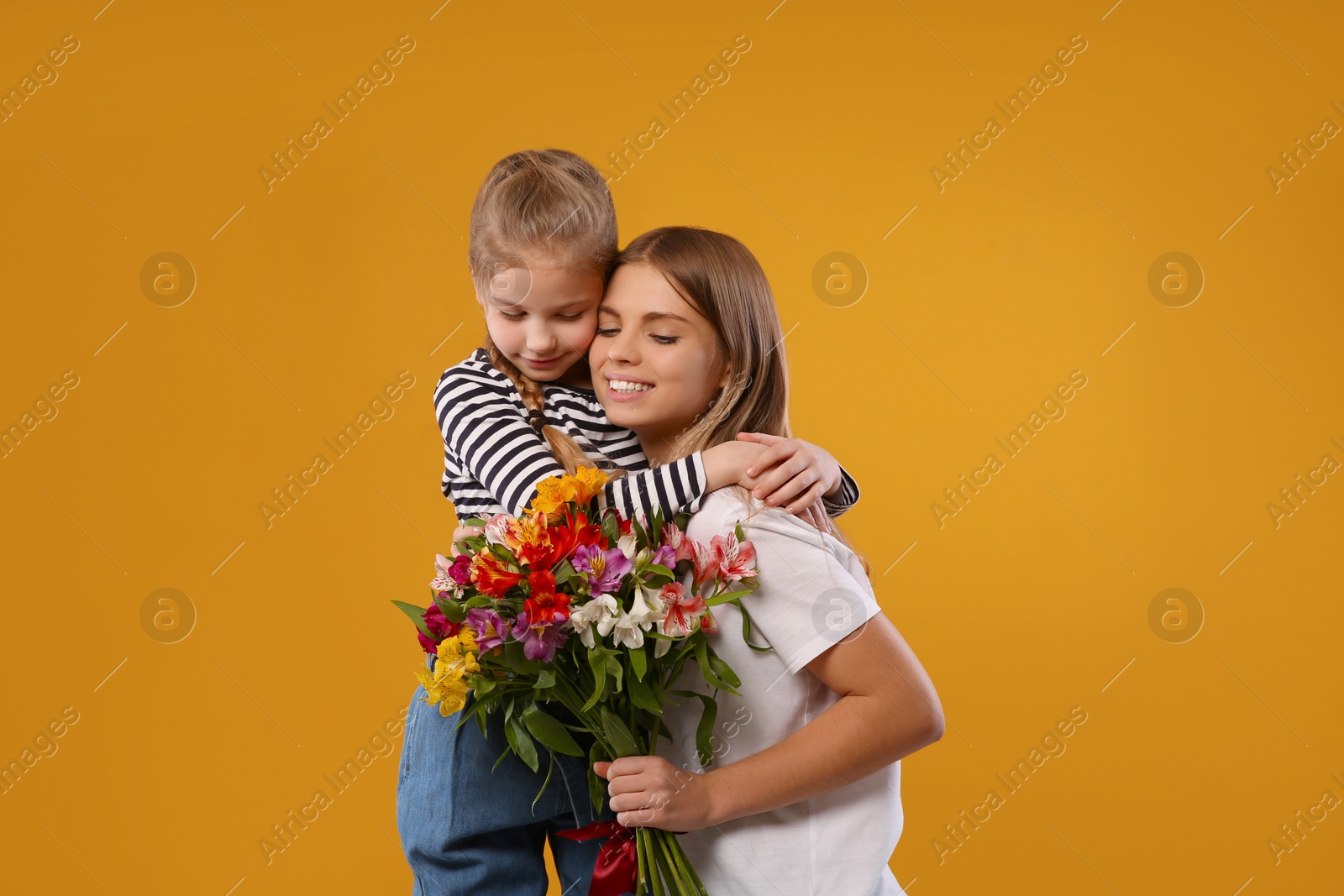 Photo of Little daughter congratulating her mom with flowers on orange background. Happy Mother's Day