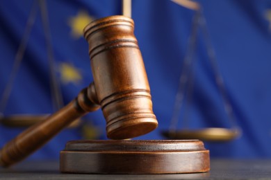 Photo of Wooden judge's gavel and Scales of justice on grey table against European Union flag, closeup