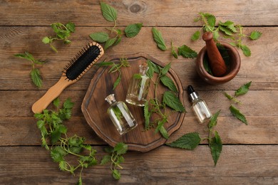 Photo of Stinging nettle extract and brush on wooden background, flat lay. Natural hair care