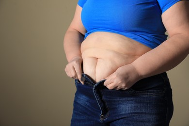 Overweight woman trying to button up tight jeans on light brown background, closeup. Space for text