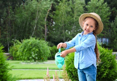 Photo of Little girl watering flowers in backyard. Home gardening