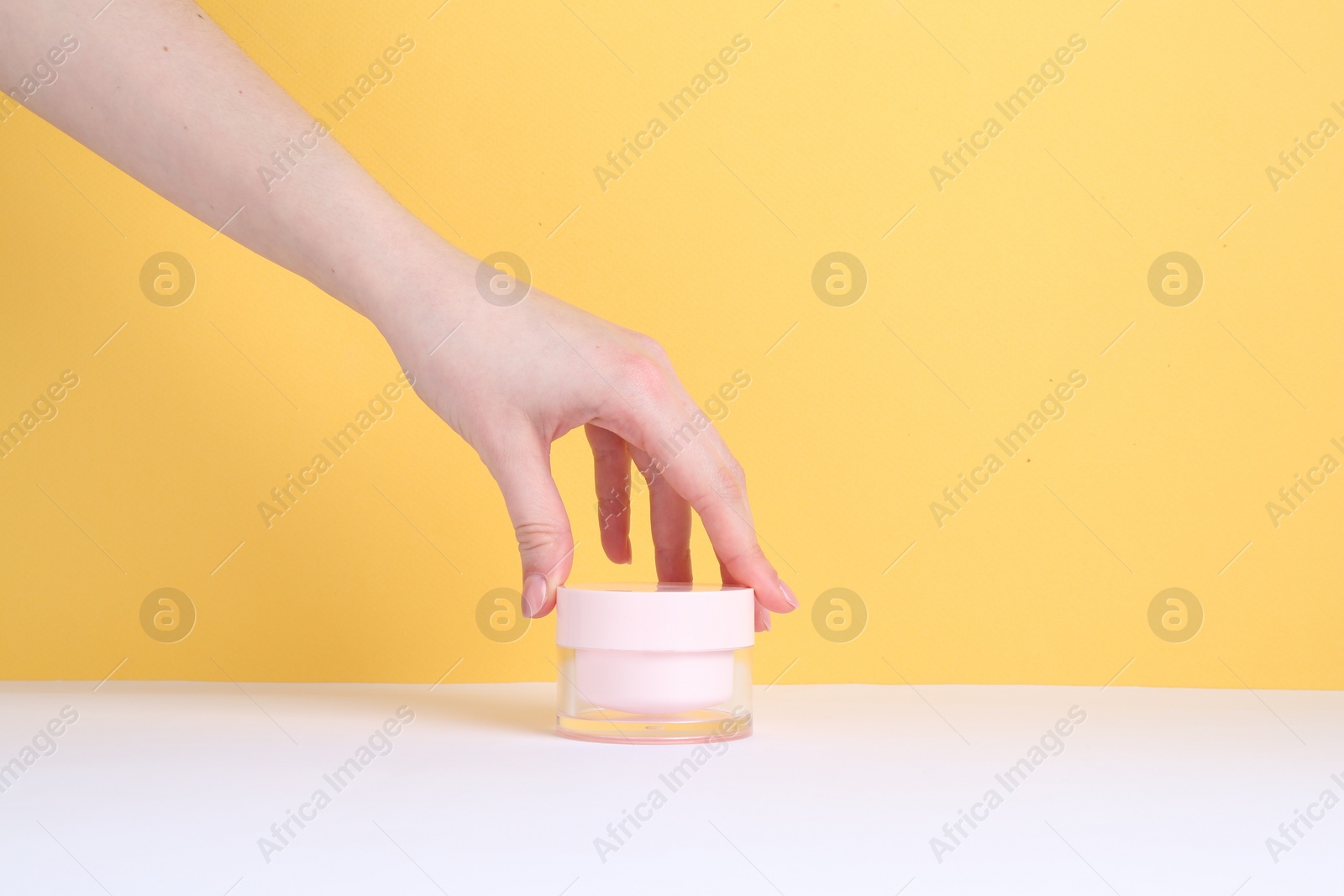 Photo of Woman with jar of cream on yellow background, closeup