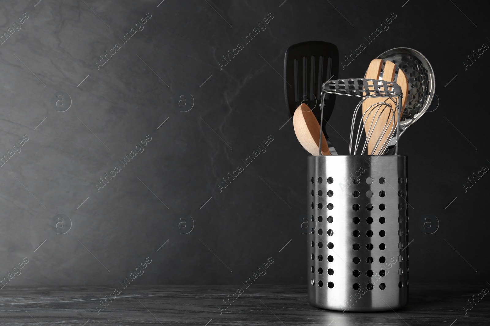 Photo of Holder with kitchen utensils on grey table against dark background. Space for text